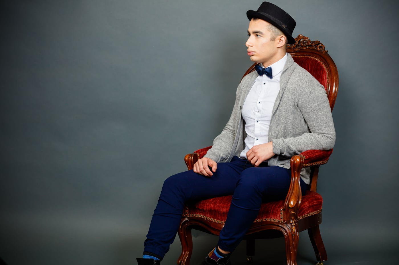 Male model hat+bowtie, red chair, teal, fashion/brand.
