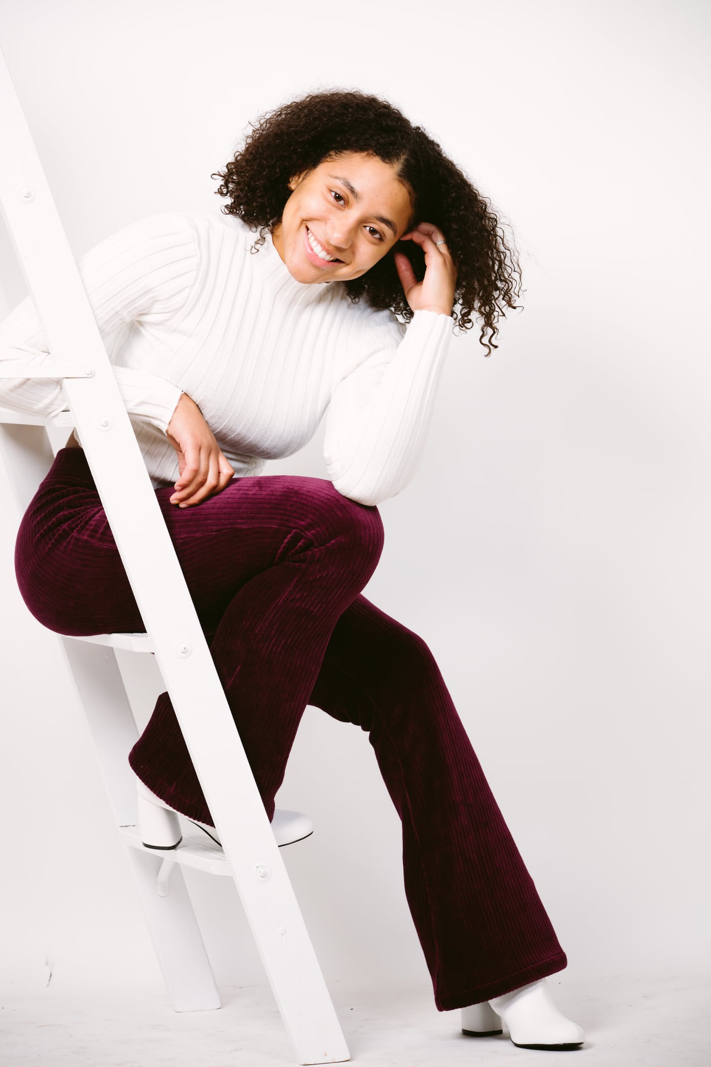 Woman white turtleneck on ladder, bright, smiling.
