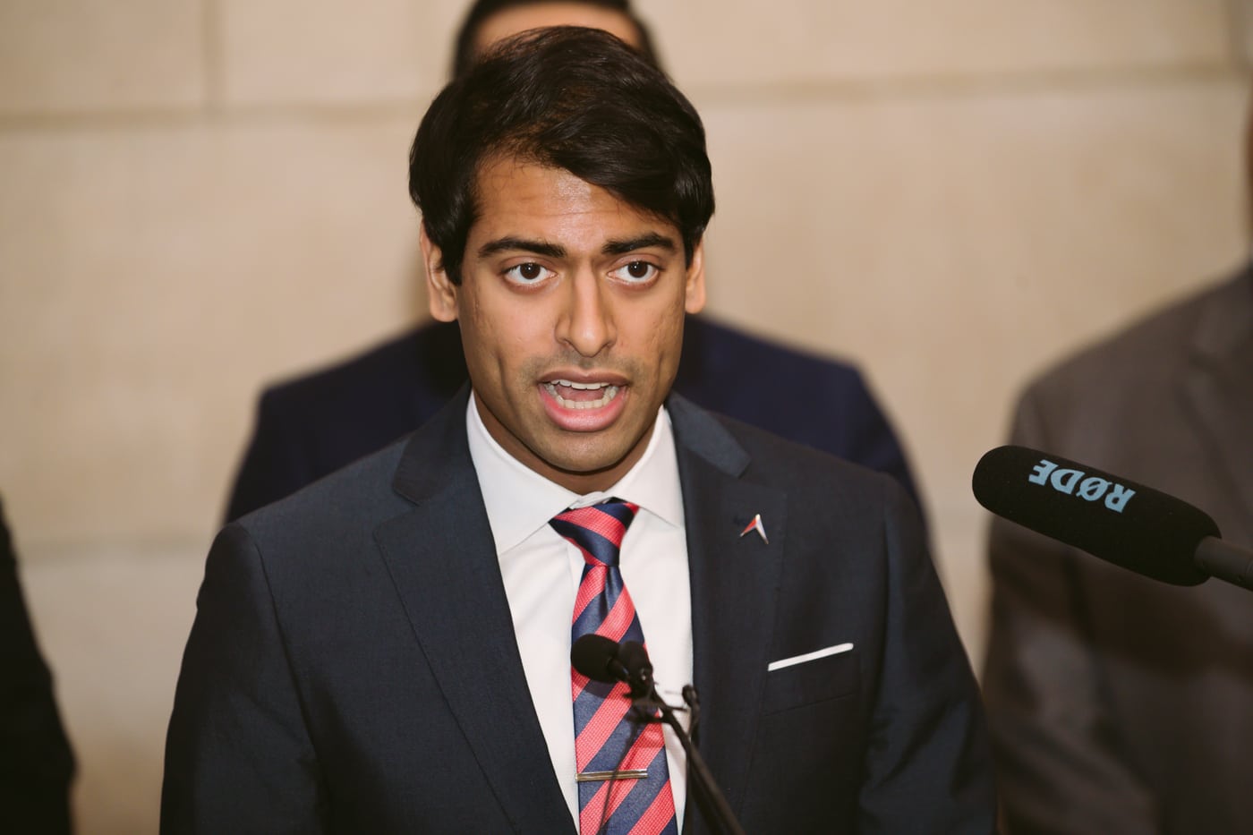 Man in suit at podium, red tie, professional/keynote.
