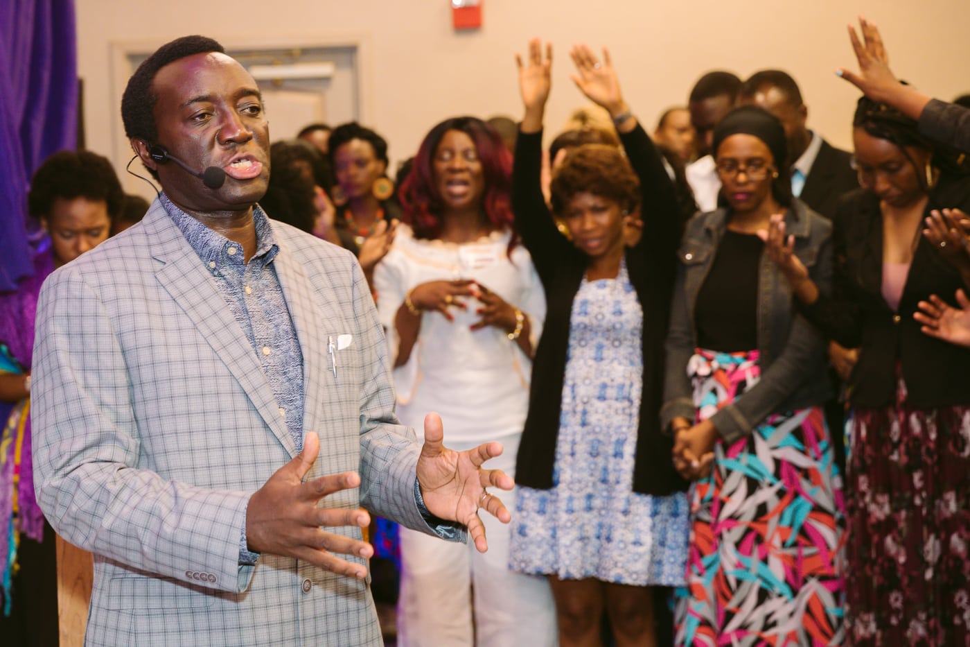 Man praying over congregation, hands raised, faith event.