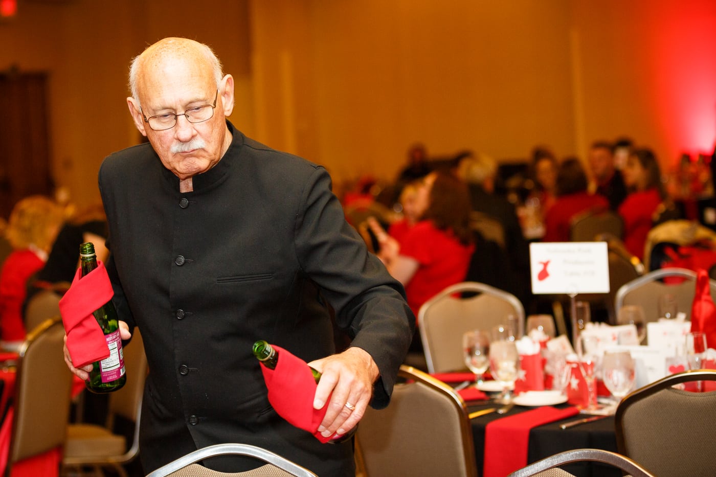 Man at red gala pouring wine, event.