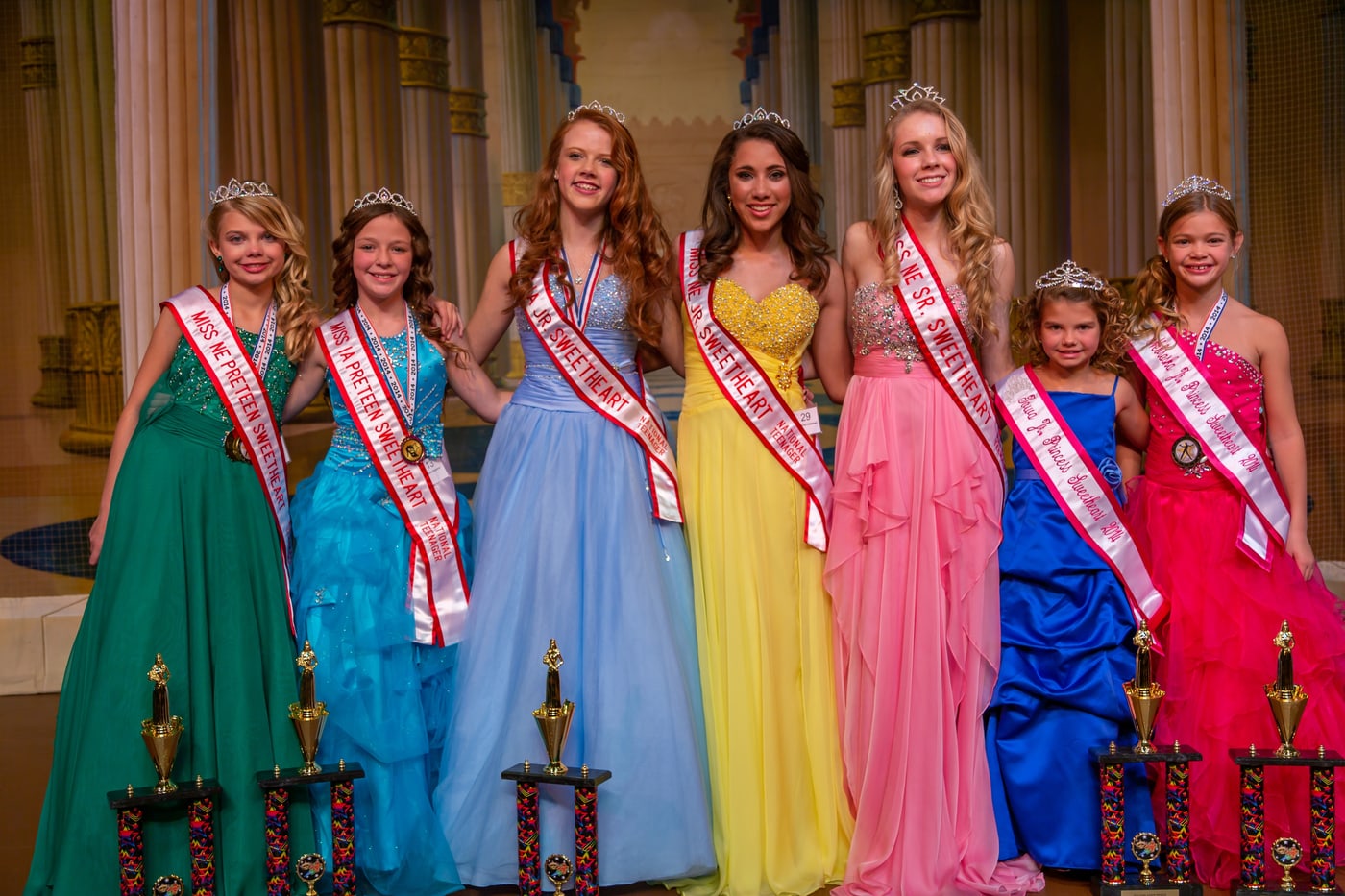 Pageant winners group with trophies and formal stage context.