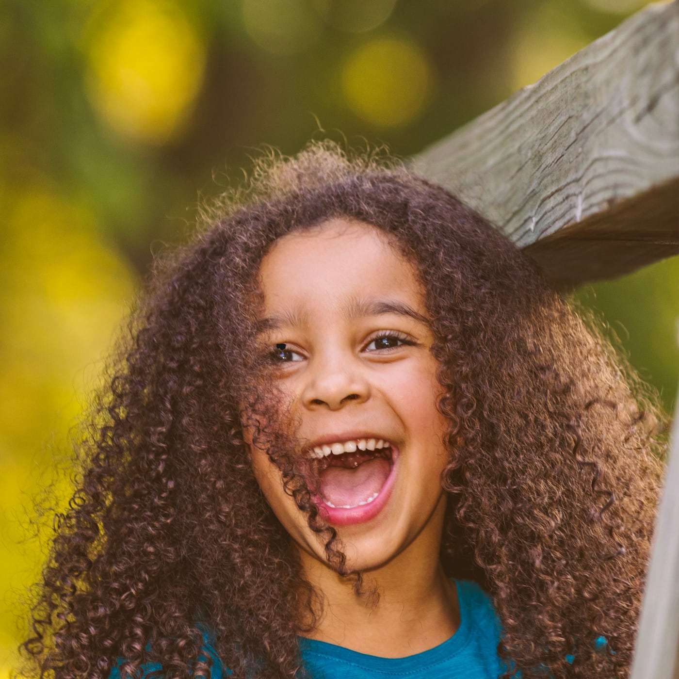 Curly-haired girl laughing big, backlit, joyful children.