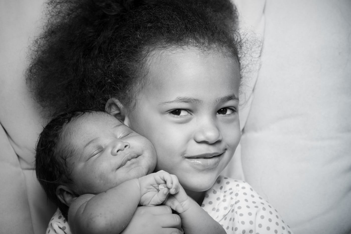 Sibling cradling newborn, B&W, tender.