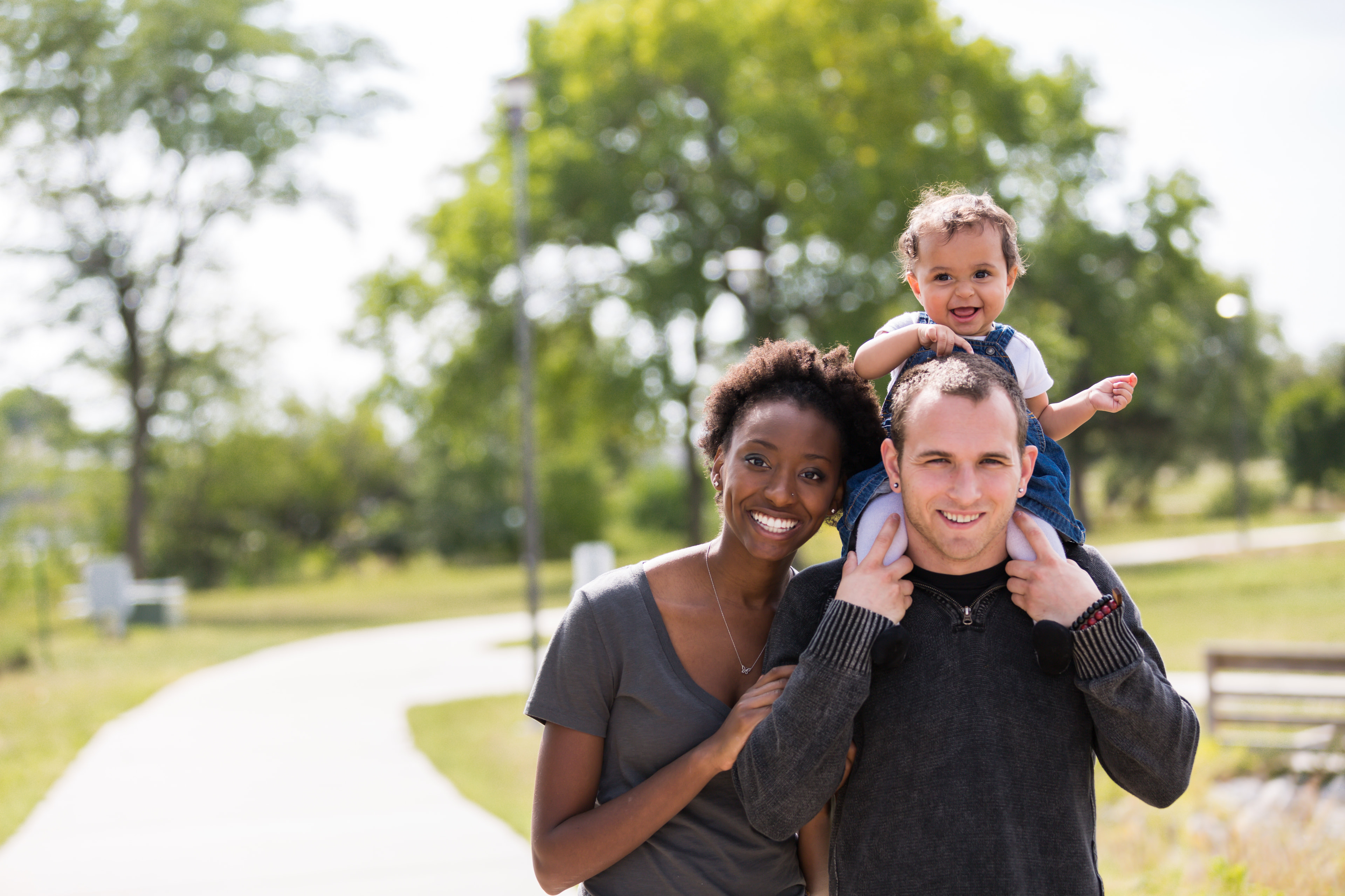 Dad with kid on shoulders, mom, park path, pure family joy.