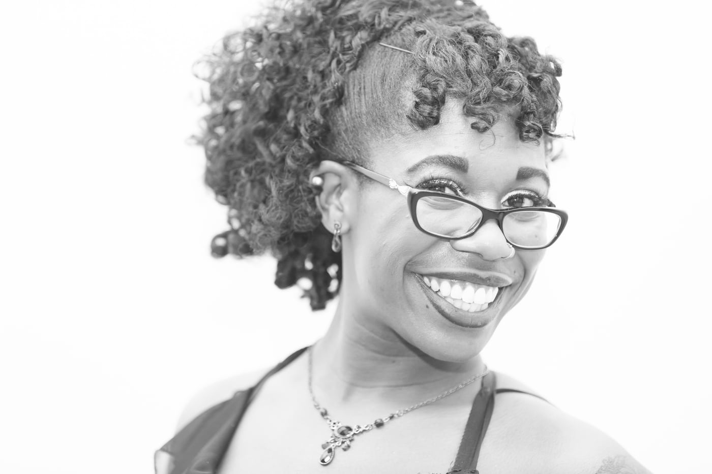 Woman curly hair + glasses, big smile, high-key.