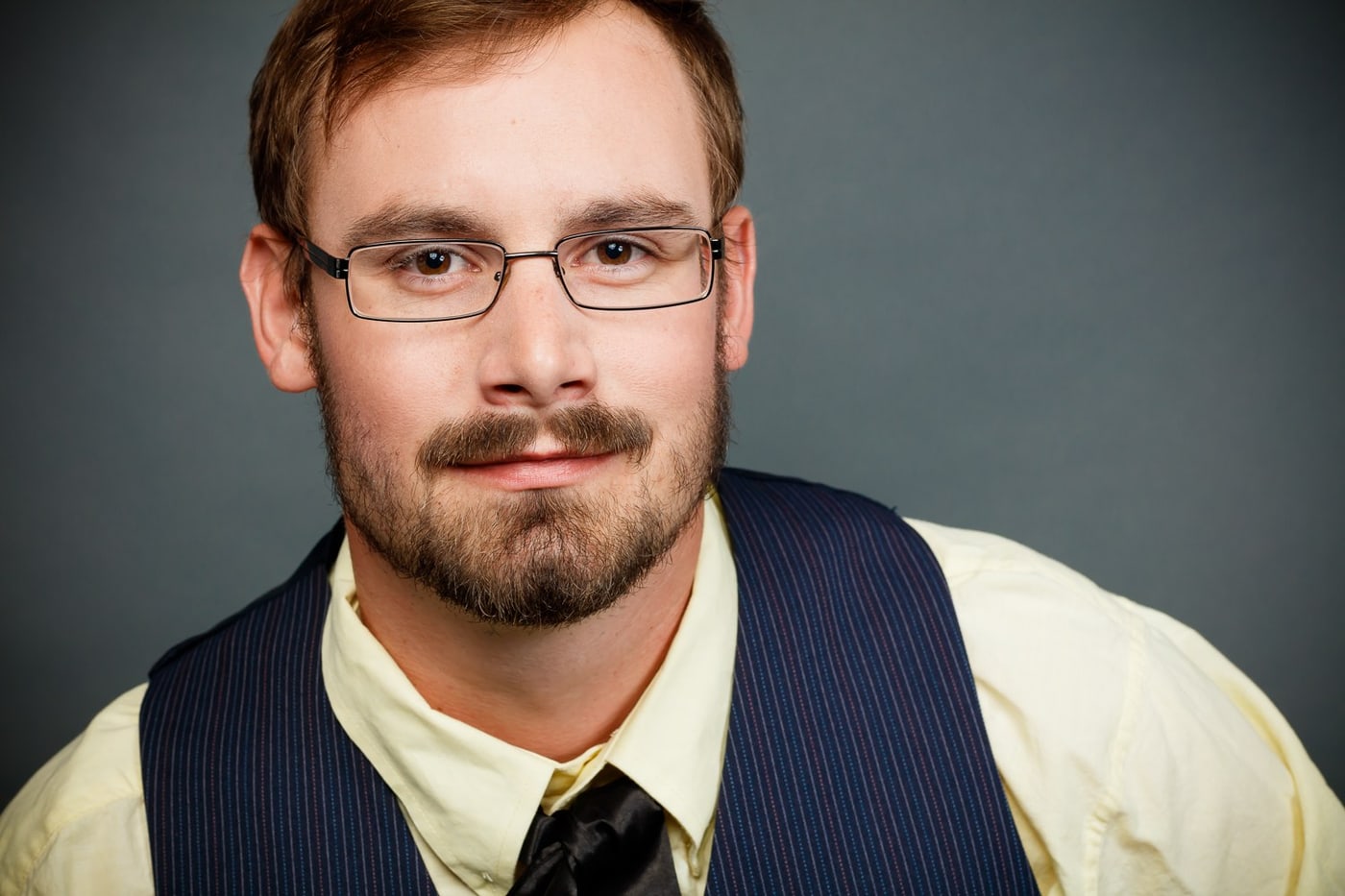 Studio male headshot with glasses and vest, direct professional presence.