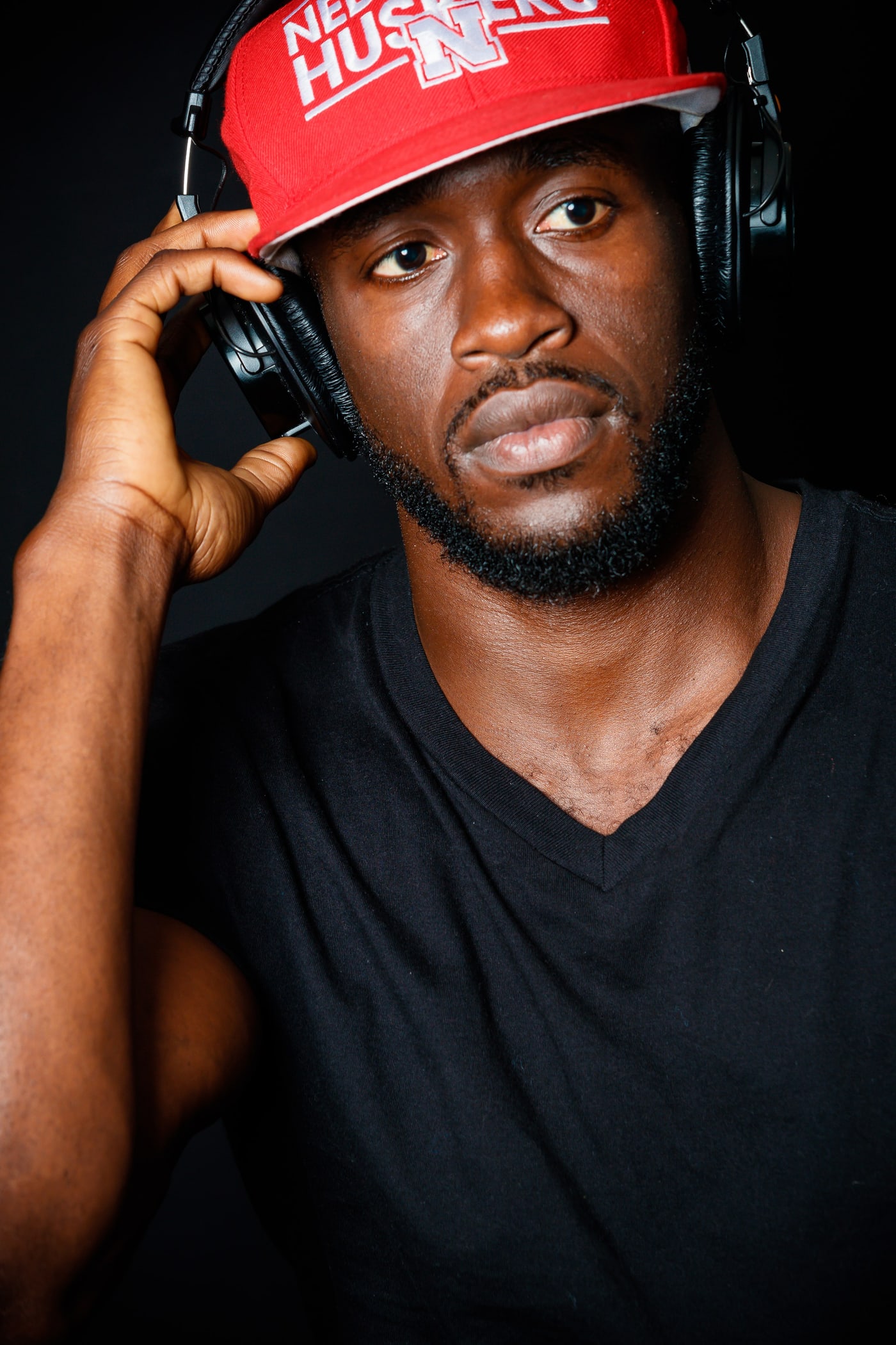Artist personal-brand portrait, black background and red cap.