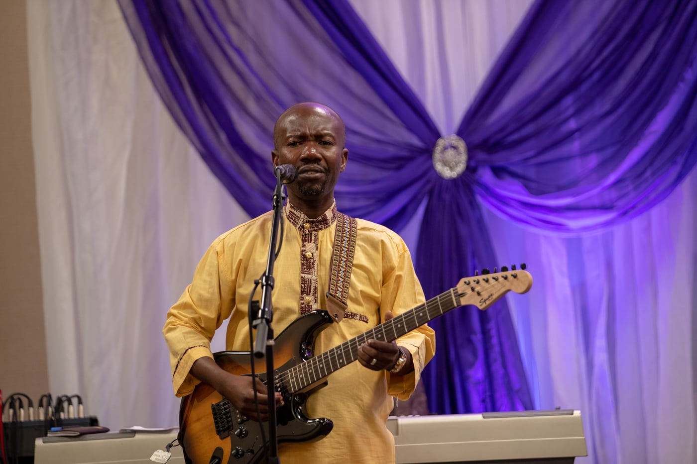 Guitarist on stage, purple drape, live music.