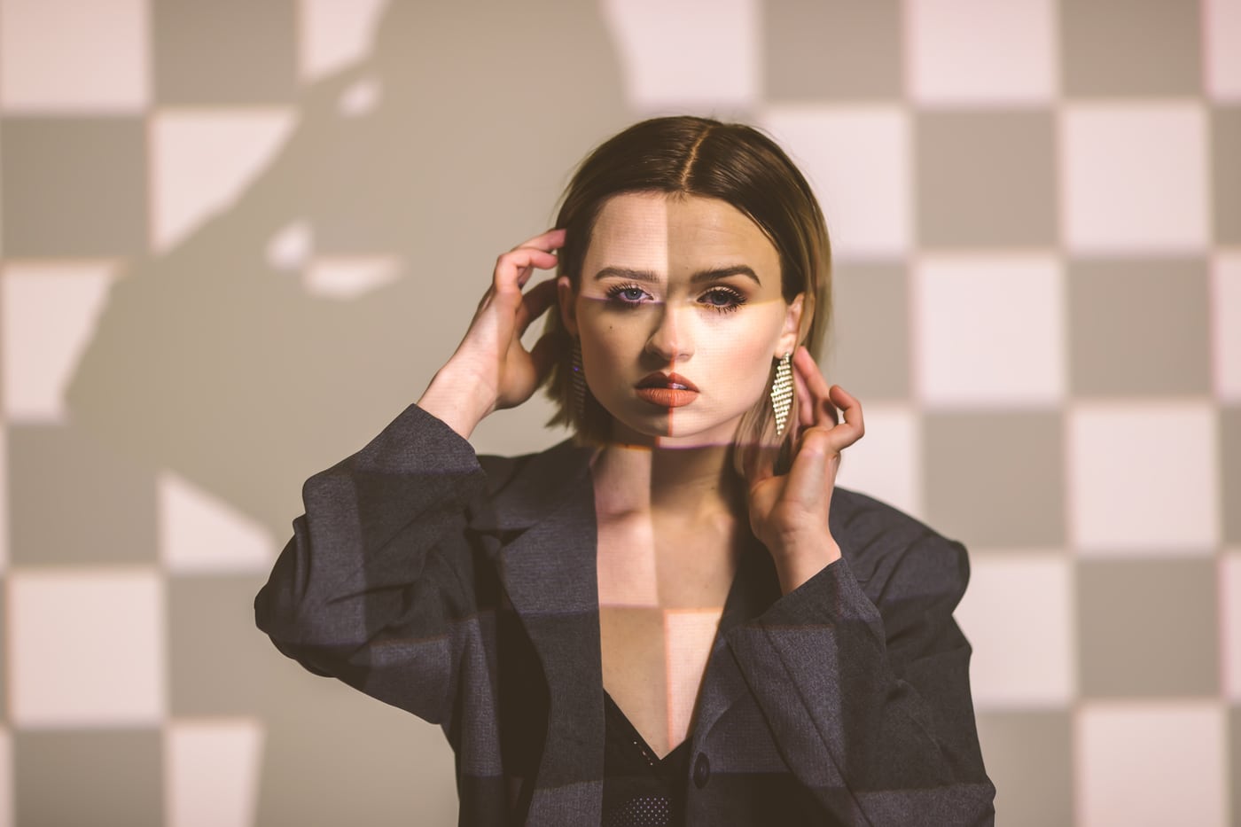 Woman on checkerboard bg, blazer, high fashion editorial.