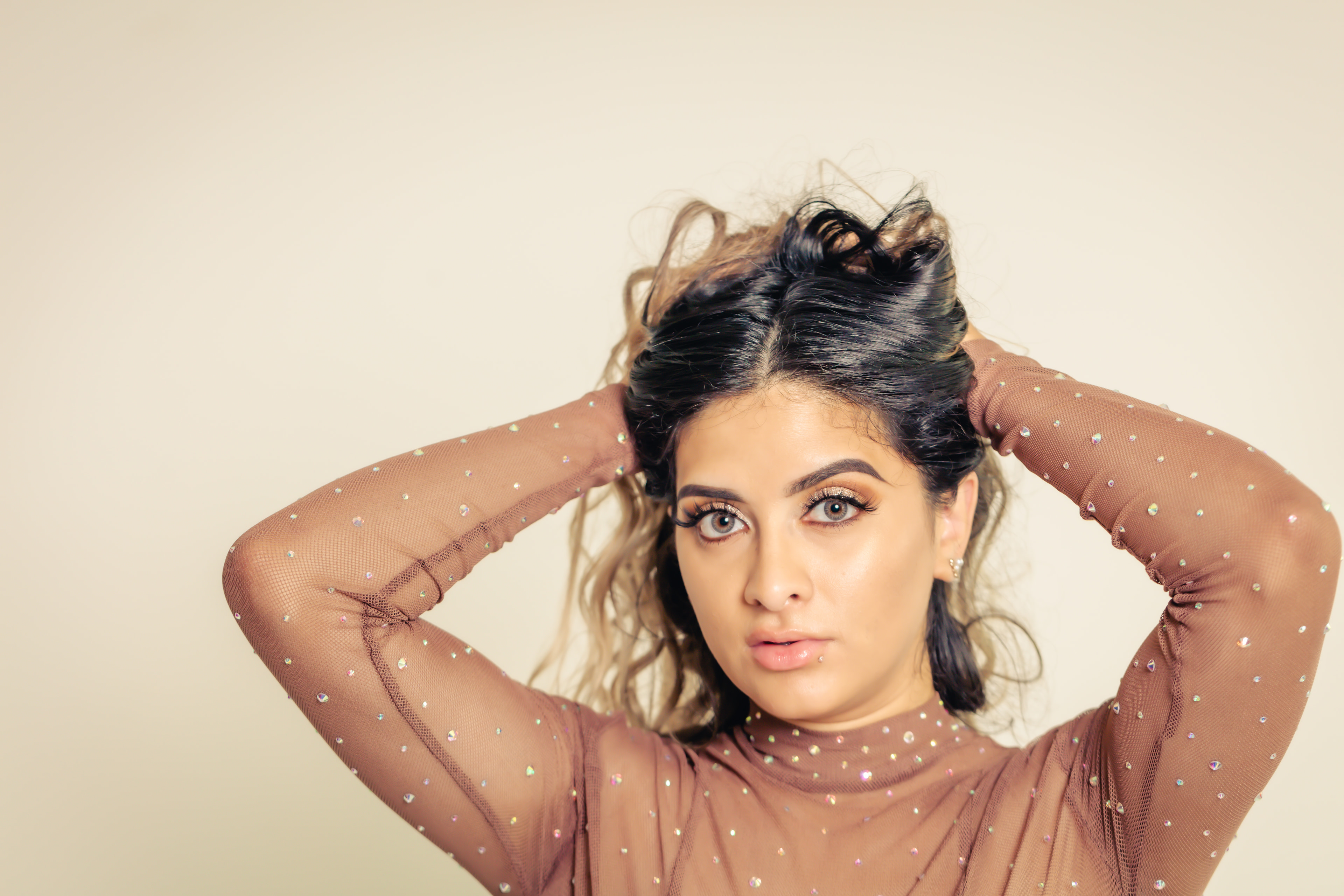 Beauty portrait, arms in hair, warm studio, polished.