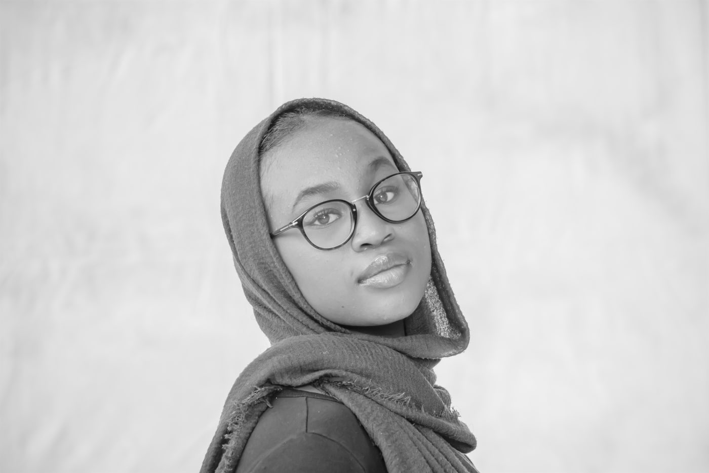 Black-and-white senior portrait with glasses and soft backdrop.