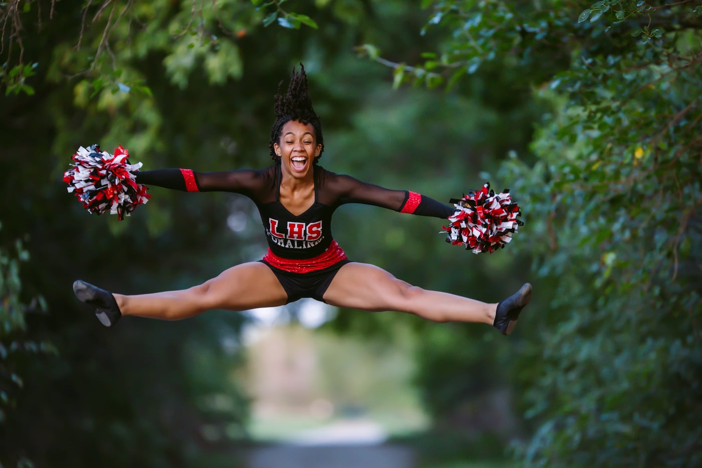 Cheerleader mid-air splits, LHS, green bokeh, peak spirit action.