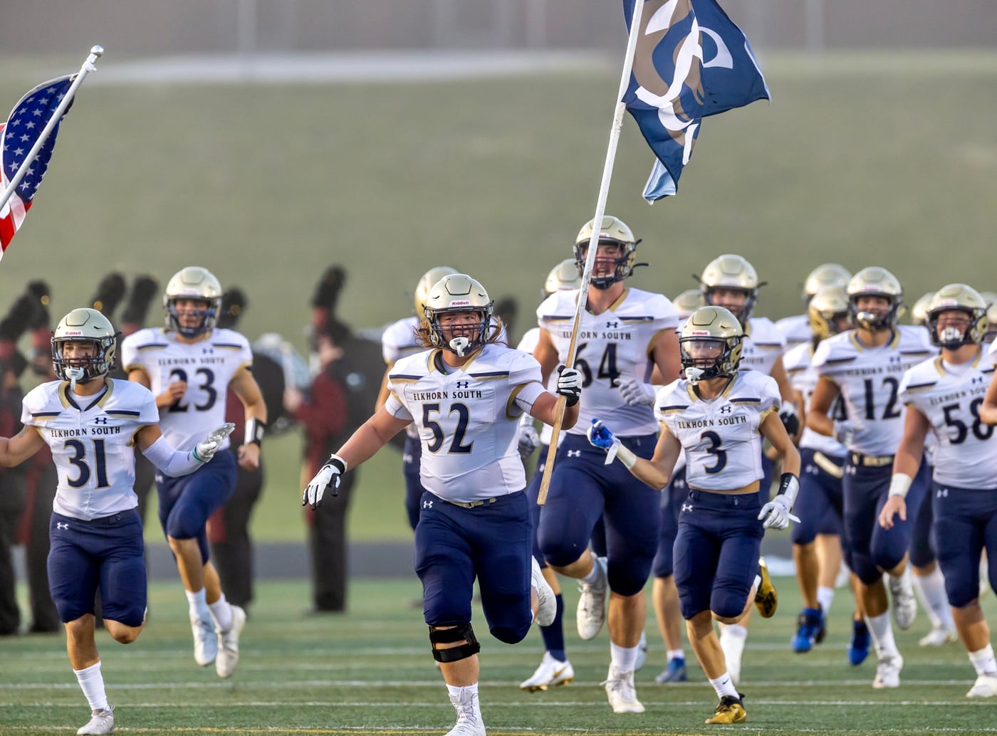 Football team running out with flags, Friday-night energy.