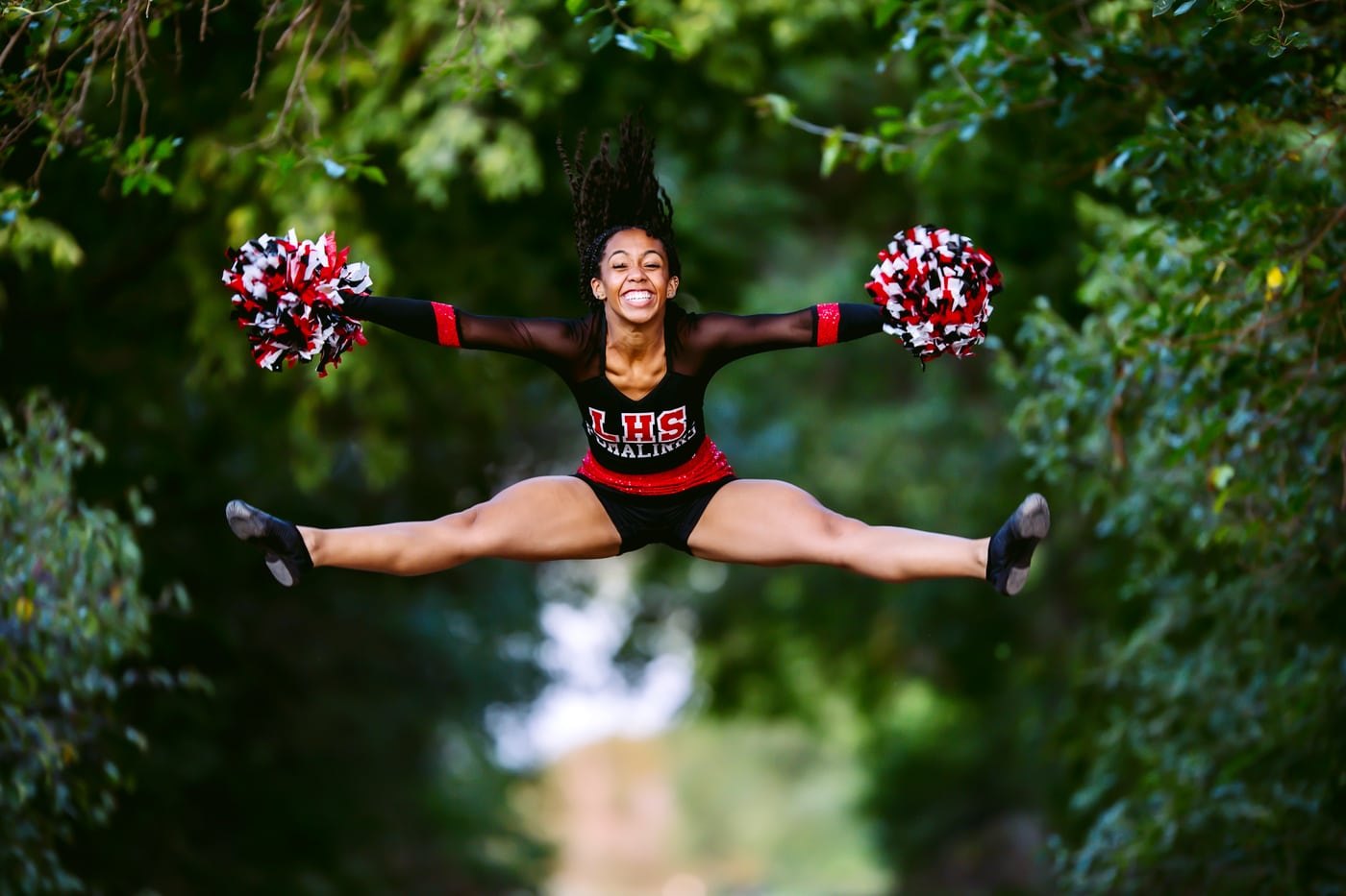 Cheerleader mid-air splits, trees, peak spirit.