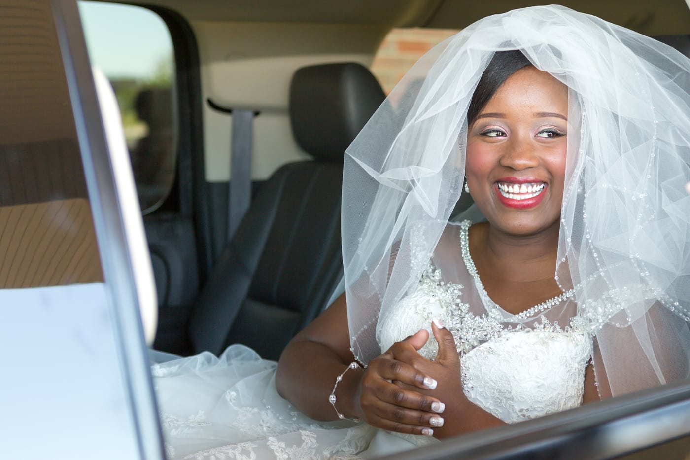 Bride in car with veil, radiant smile.