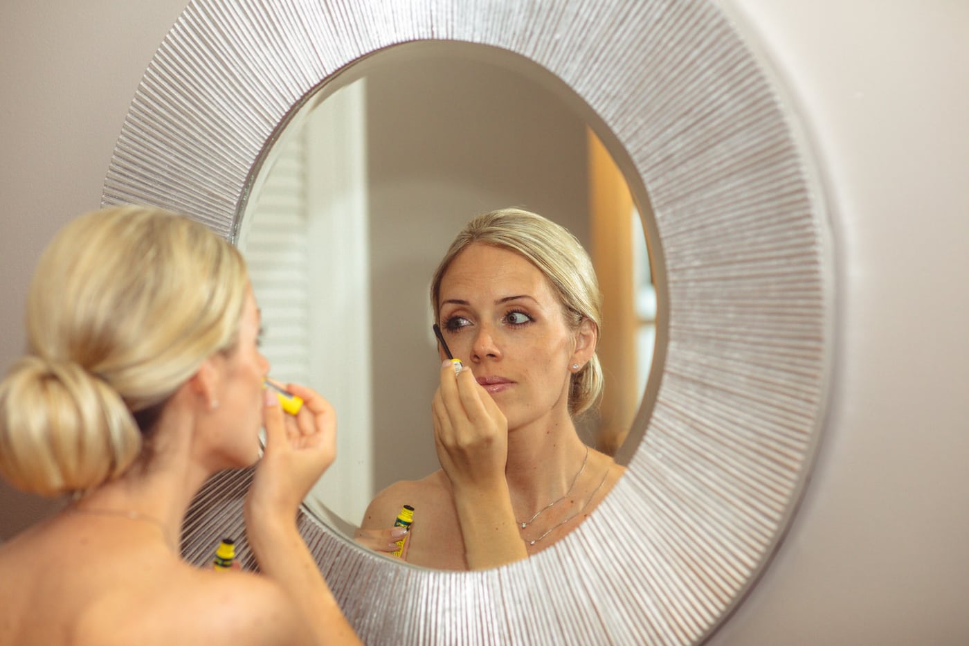 Bride applying makeup in round mirror, prep.