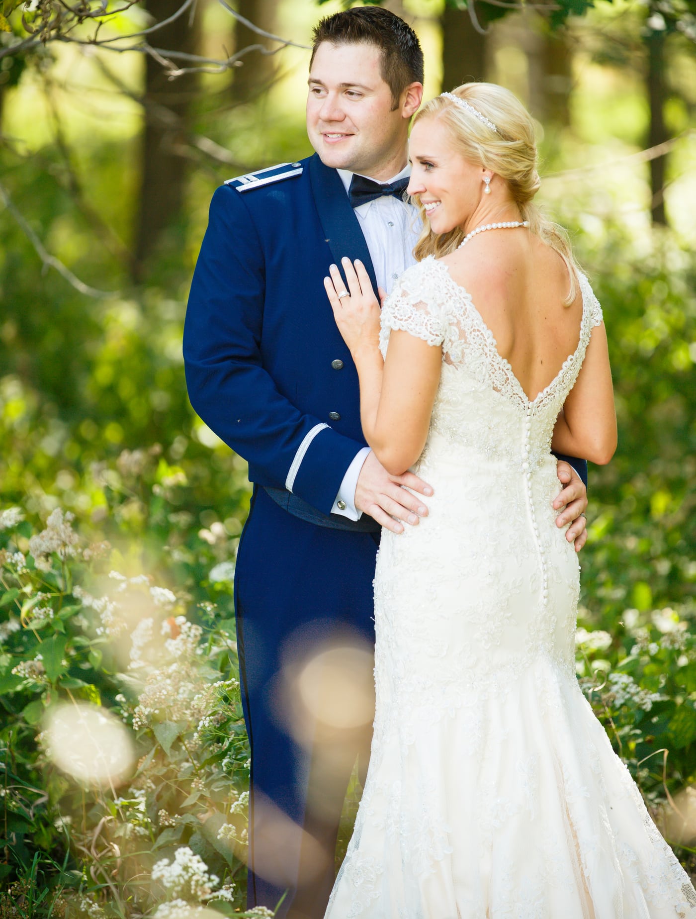 Military groom + bride, garden embrace.