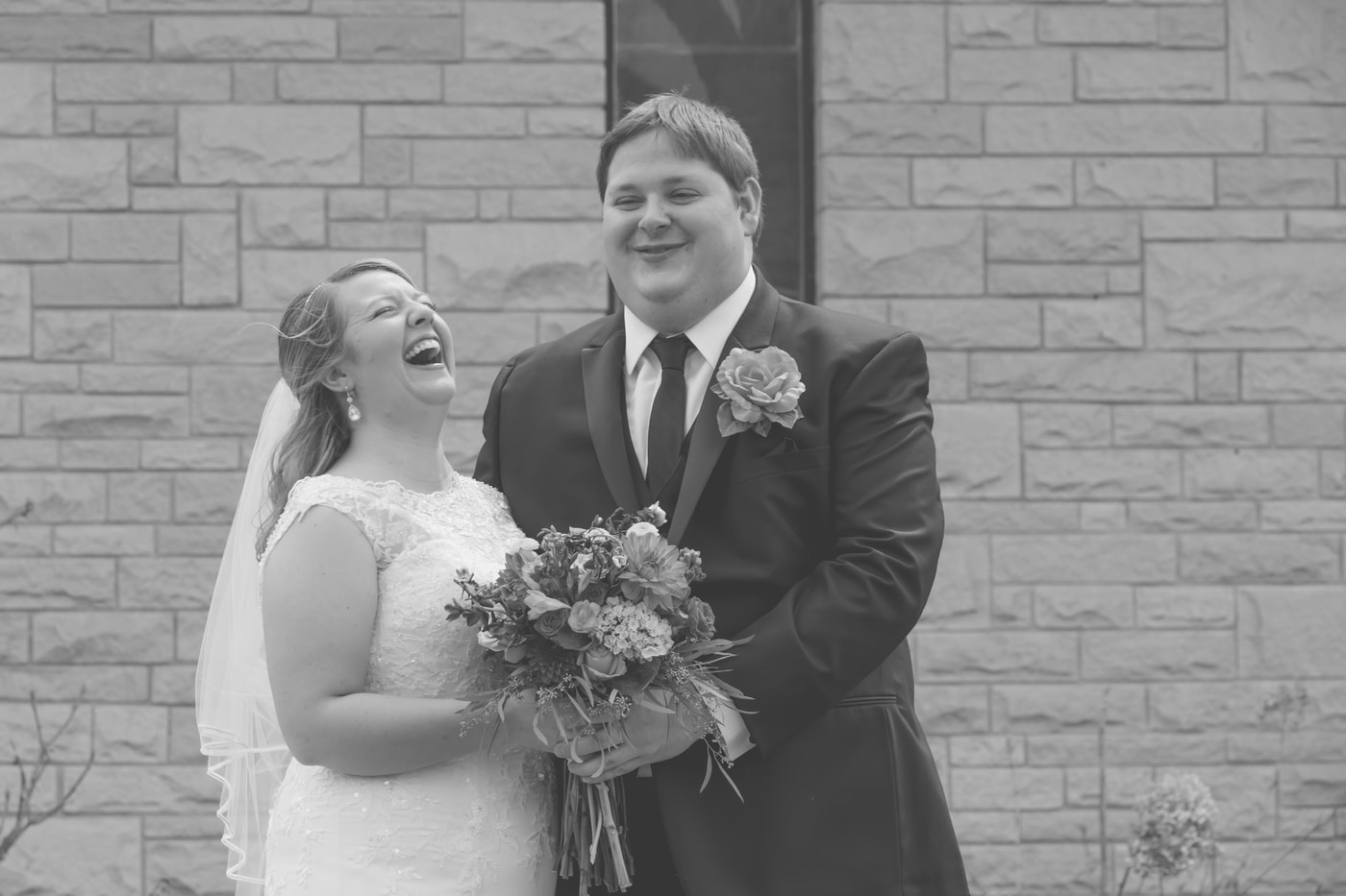 Wedding couple laughing with bouquet.