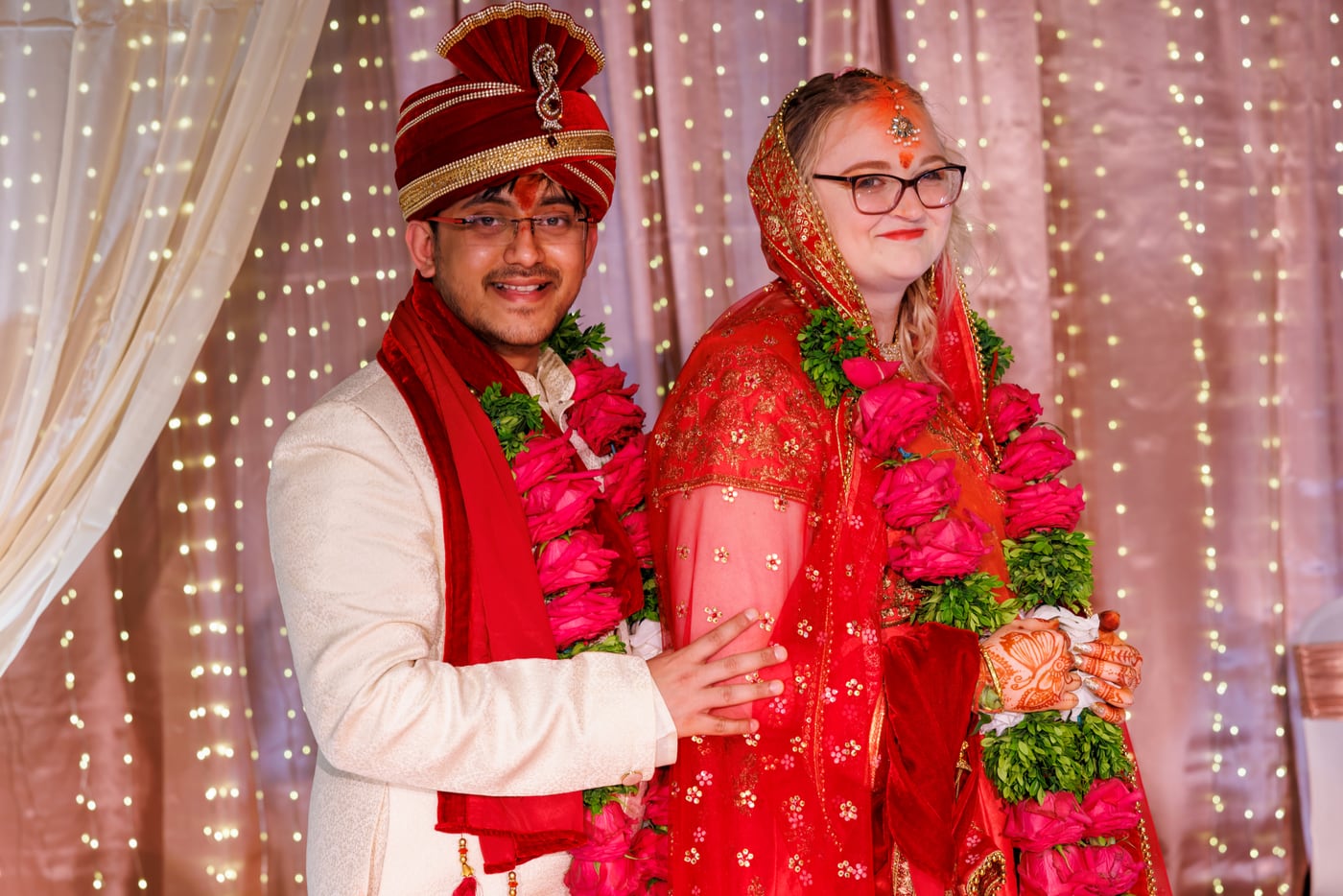 Wedding couple in vivid traditional attire framed by reception lights.