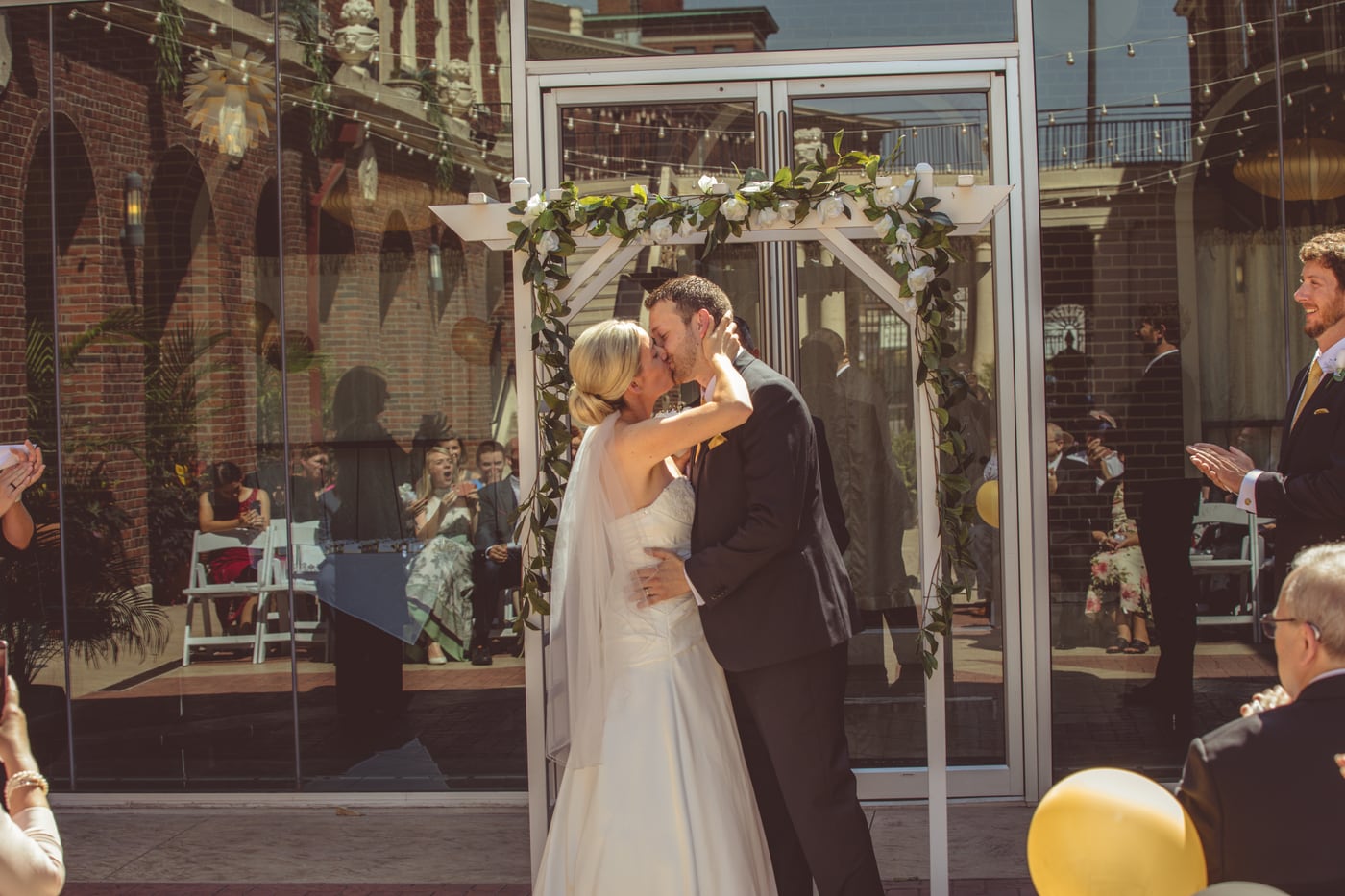 Wedding ceremony procession with the couple framed by guests and warm architectural detail.