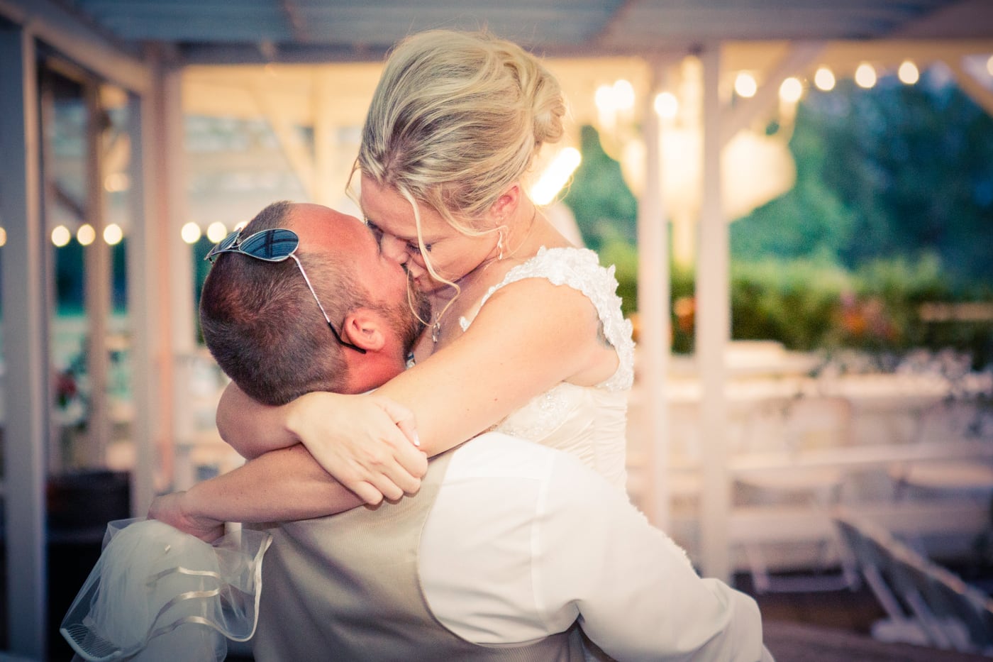 Newlyweds sharing a joyful kiss in warm outdoor light.