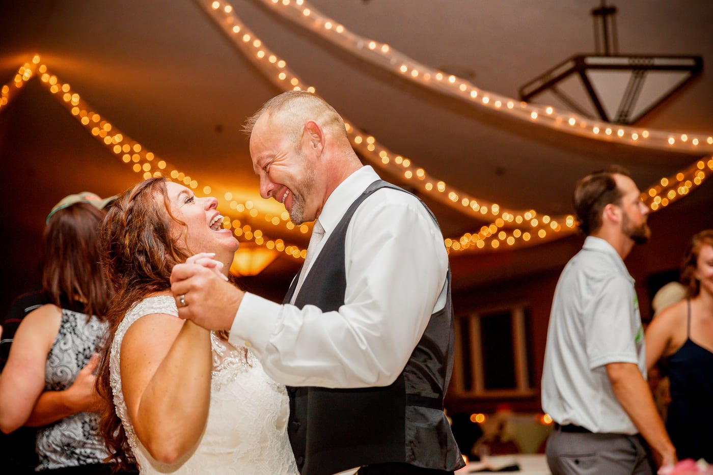 Couple dancing under warm string lights at a wedding reception.